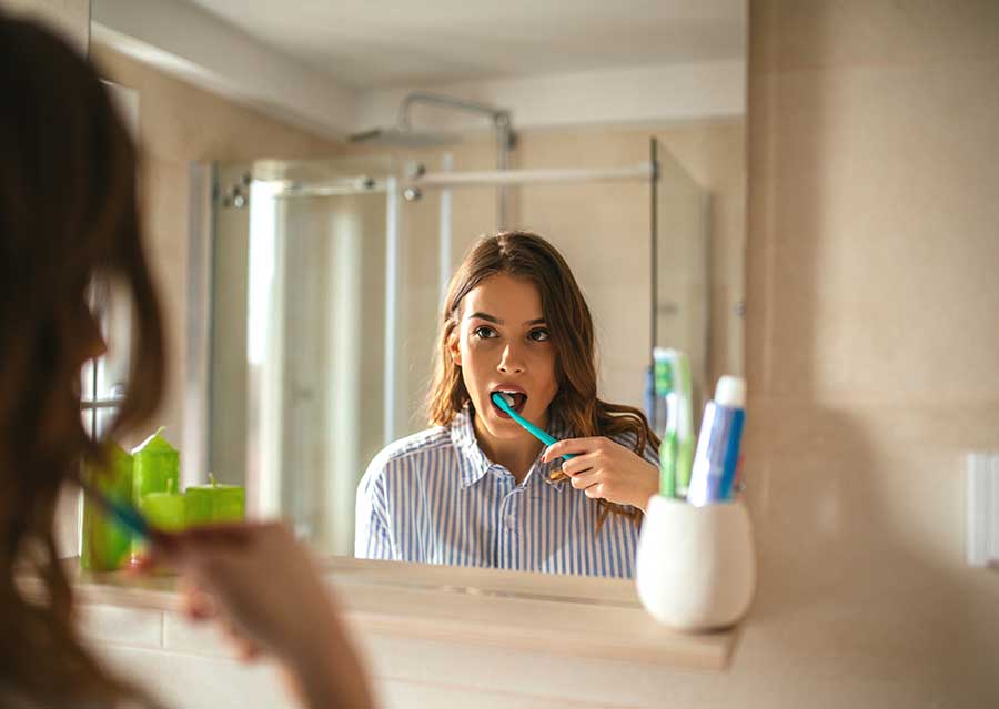 Retrato de una mujer hermosa que se cepilla los dientes y se mira en el espejo del baño.