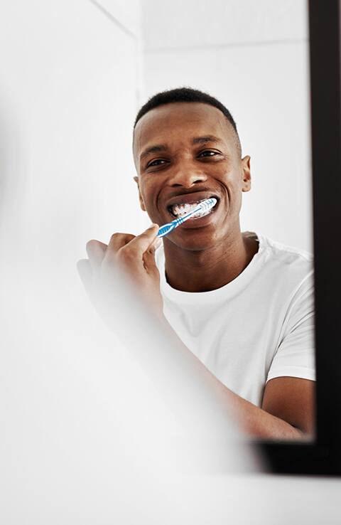 man brushing teeth in mirror with Colgate toothbrush